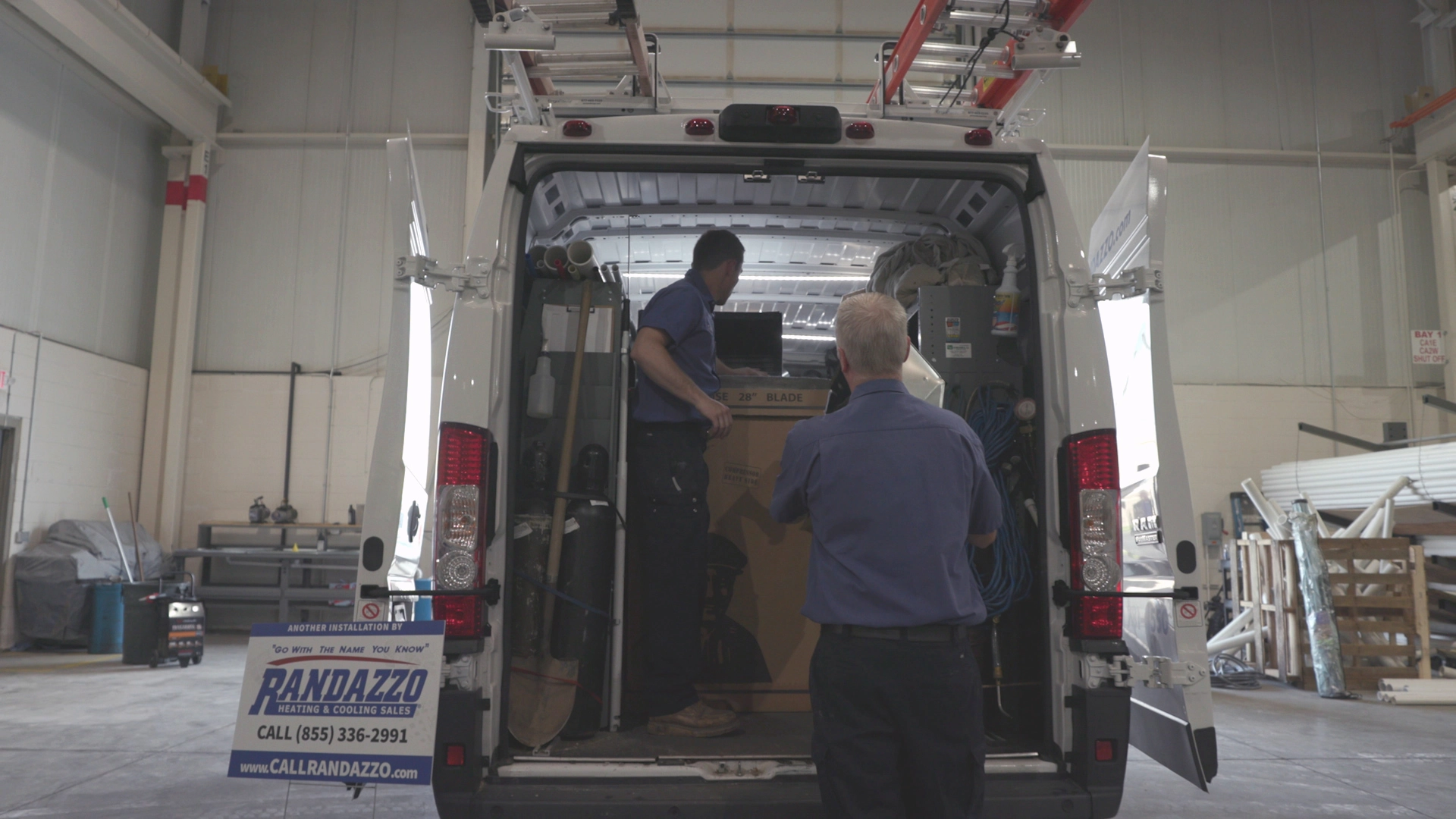 2 Randazzo employees loading the back of a company van with air conditioning replacement units