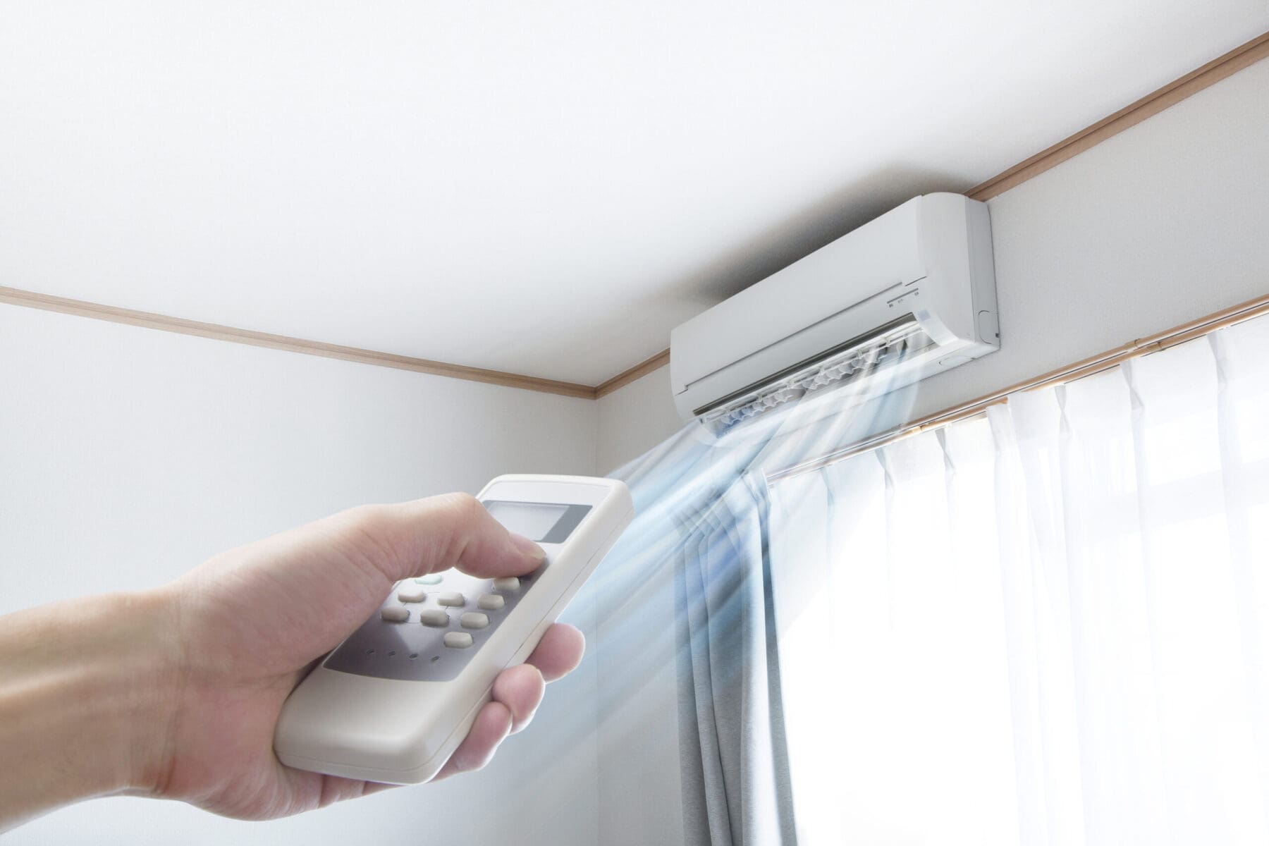 Woman’s hand with remote pointing at ductless mini-split blowing air