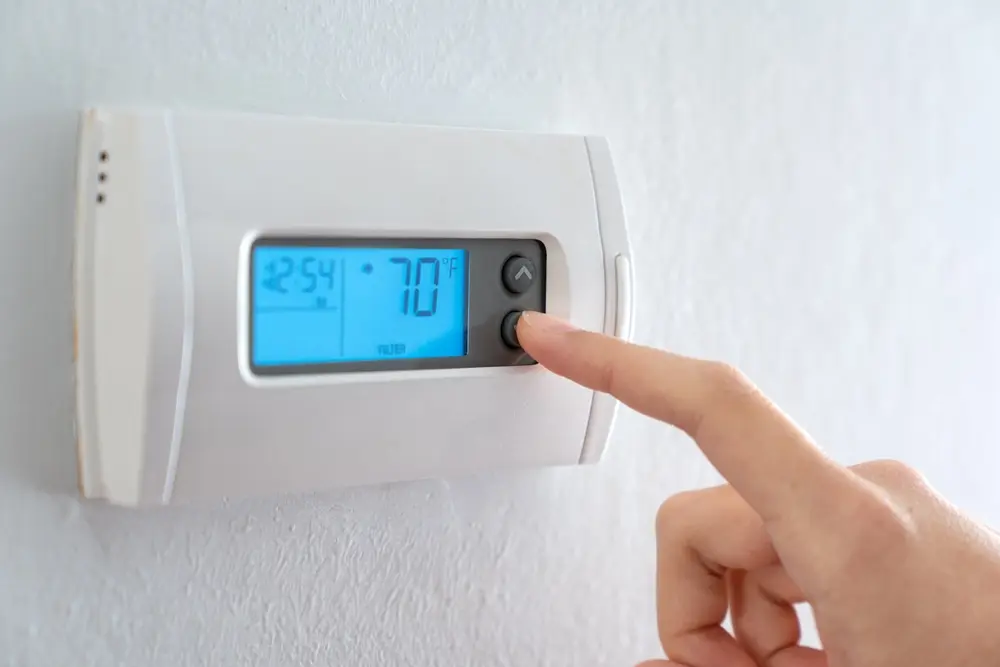 a woman pressing the down button of a house thermostat