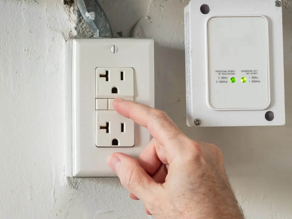 a hand pressing a gfci outlet reset button on a wall